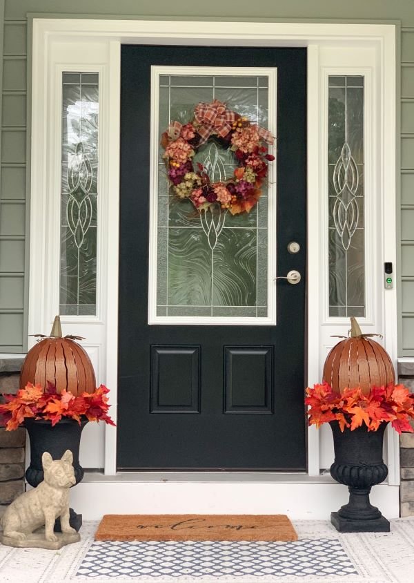 Fall Front Porch with beautiful autumn wreath, metal pumpkins, leaves sitting in black urns.