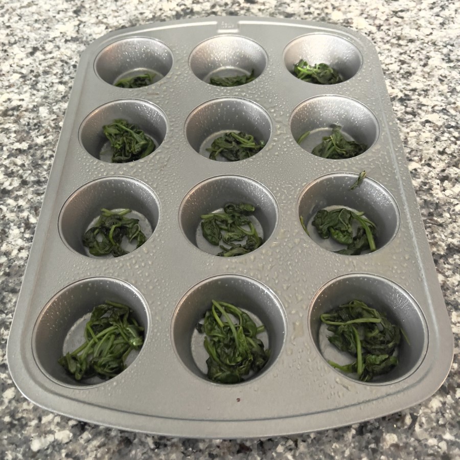 Cooked Spinach added to muffin pan for the start of making spinach & Feta Egg Bites.