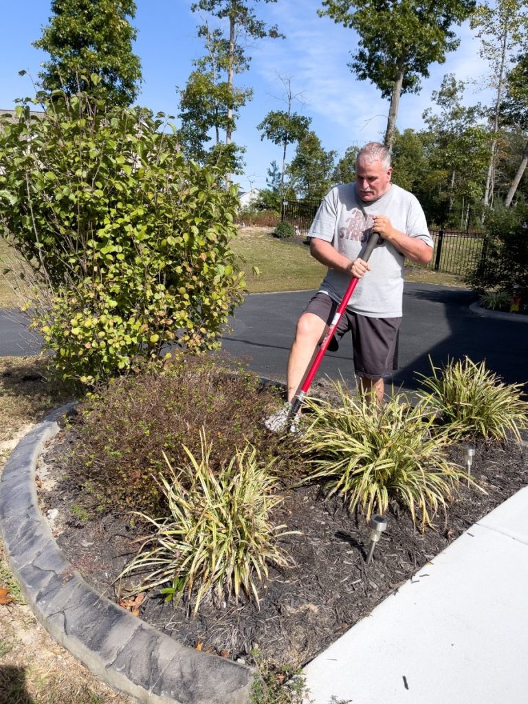 A man working with a shovel to dig up plants. He is working on creating a better landscape.