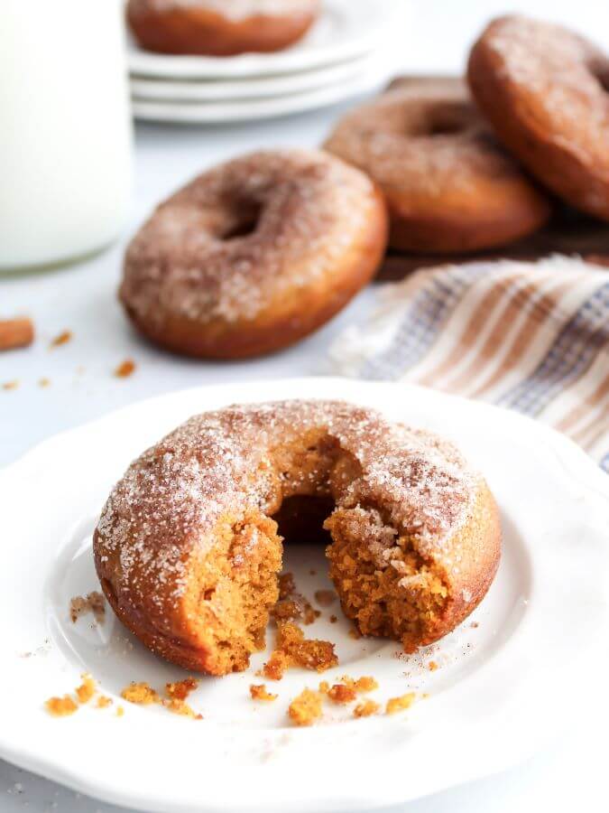 Pumpkin Spiced Donuts with one on white plate with a piece missing. A perfect recipe for fall.