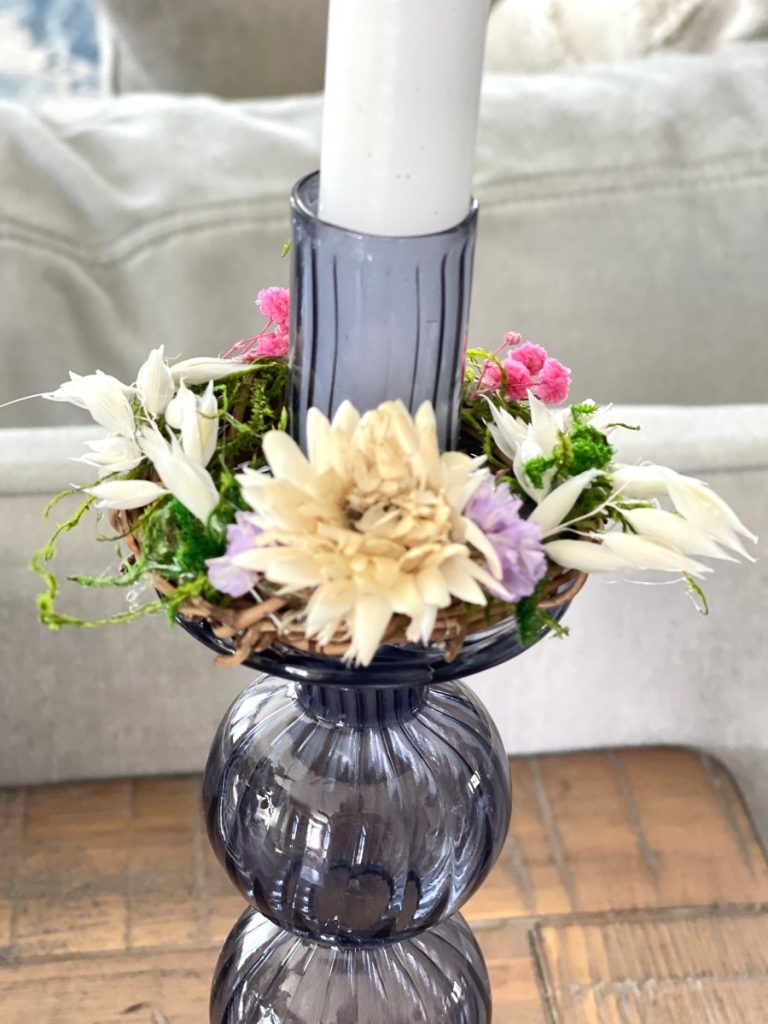 DIY candle ring with grapevine wreath, dried flowers and moss on a glass blue candle holder with white taper candle.