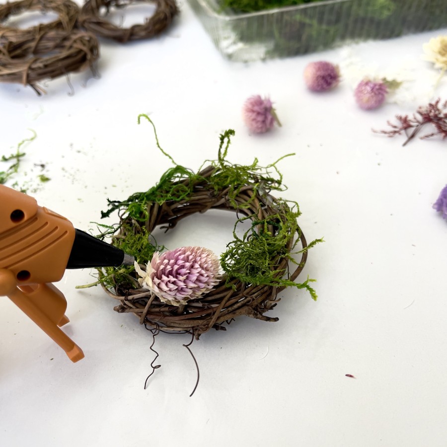 Hot glue gun used for applying hot glue to a 3-inch grapevine wreath with moss and dried flowers.