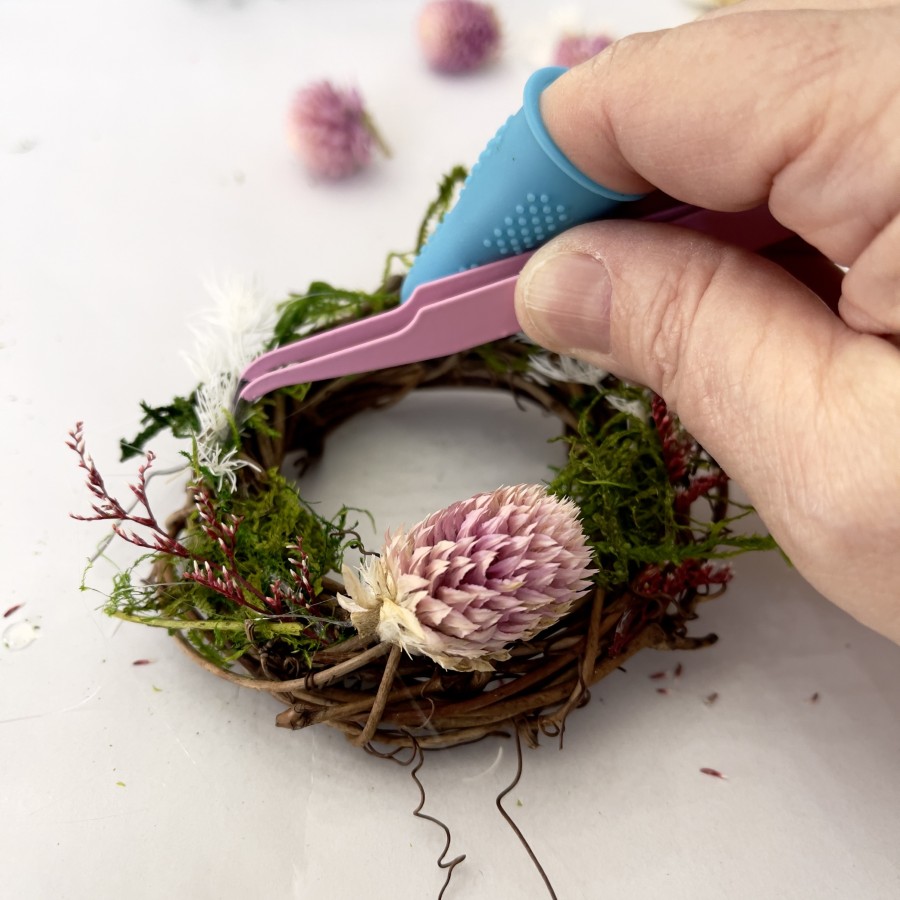 Adding dried flowers to a small grapevine wreath covered with moss.